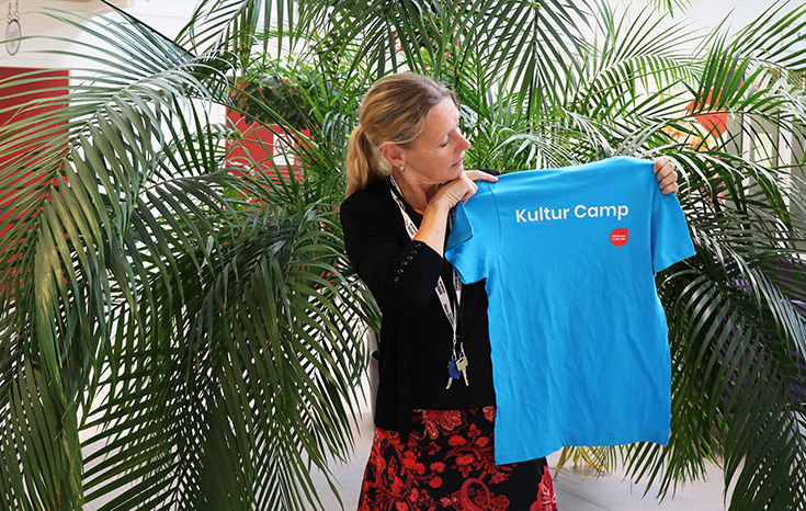 Kvinna som håller upp en blå t-shirt där det står "Kultur camp".